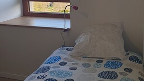 Ein Schlafzimmer mit Fenster, einem Bett mit gemusterten Betttextilien und einem an der Wand montierten Thermostat.