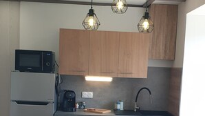Eine moderne Küche mit Holzschränken, einem Edelstahlkühlschrank, einer Mikrowelle, einer Kaffeemaschine und Pendelleuchten.