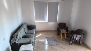 Une pièce comprenant un canapé, un fauteuil, une petite table et une fenêtre avec des stores.