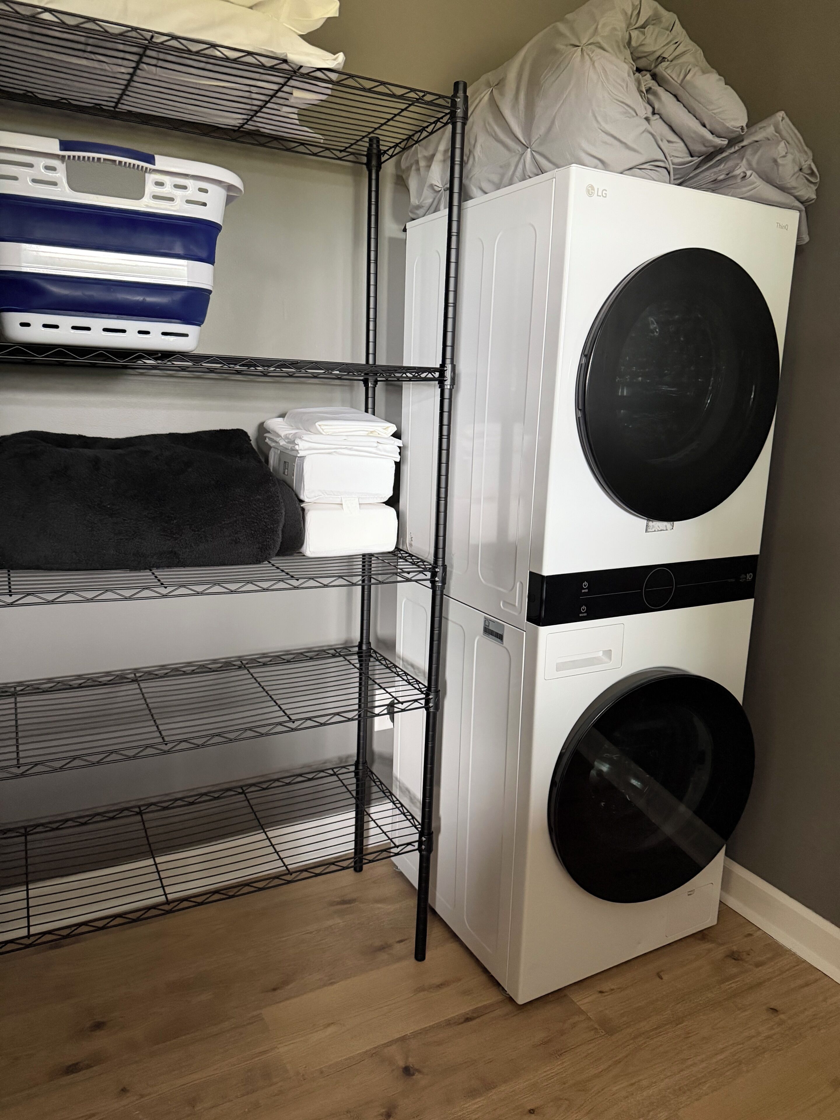 A laundry area with stacked washers and dryers, shelves with folded towels, and a basket.