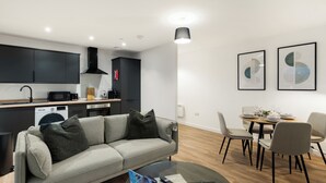A modern kitchen with dark cabinets, a dining area with a round table and chairs, a gray sofa with cushions, and two framed abstract art pieces on the wall. - City Point Aberdeen by Guestz (Aberdeen)