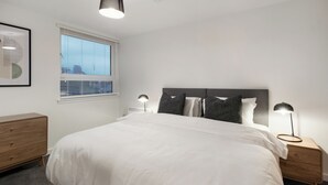 A bedroom with a bed, bedside lamps, a nightstand, a dresser, a window with blinds, and a ceiling light fixture. - City Point Aberdeen by Guestz (Aberdeen)