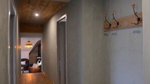 A hallway with wooden flooring, a ceiling with exposed beams, a hanging light fixture, and a coat rack with hooks. - Farm Cottage - "Le Perchoir" (Passenans)