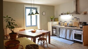 A kitchen with a dining table, chairs, a potted plant, a clock, and a stove. - Farm Cottage - "Le Perchoir" (Passenans)