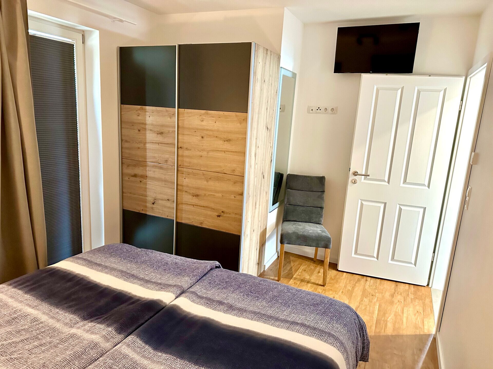 A bedroom with a bed, a wardrobe, a chair, and a TV.