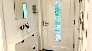 En vit dörr med ett frostat glasparti, en vit spegel som hänger på väggen och ett vitt skåp med lådor och en vas med blommor.