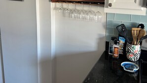 Une cuisine avec une étagère en bois où sont posés des verres à vin, un tableau encadré au mur et divers ustensiles de cuisine sur le plan de travail.
