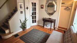 Un escalier menant à un palier où se trouvent une porte, un miroir, une petite table, un banc et une plante en pot.