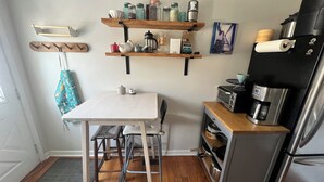 Une cuisine compacte avec une table blanche, des tabourets, une machine à café, un four à micro-ondes et un réfrigérateur.