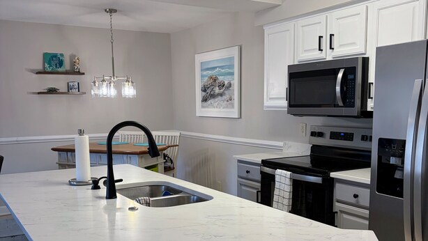 A modern kitchen with a large island, stainless steel appliances, and a pendant light. - Clean and like new condo in Calabash with amazing views of the golf course. (Calabash)