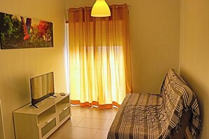 Ein Zimmer mit Fernseher auf einem Schrank, einer Couch mit gemustertem Bezug, einem Vorhang und einem Vogelbild.