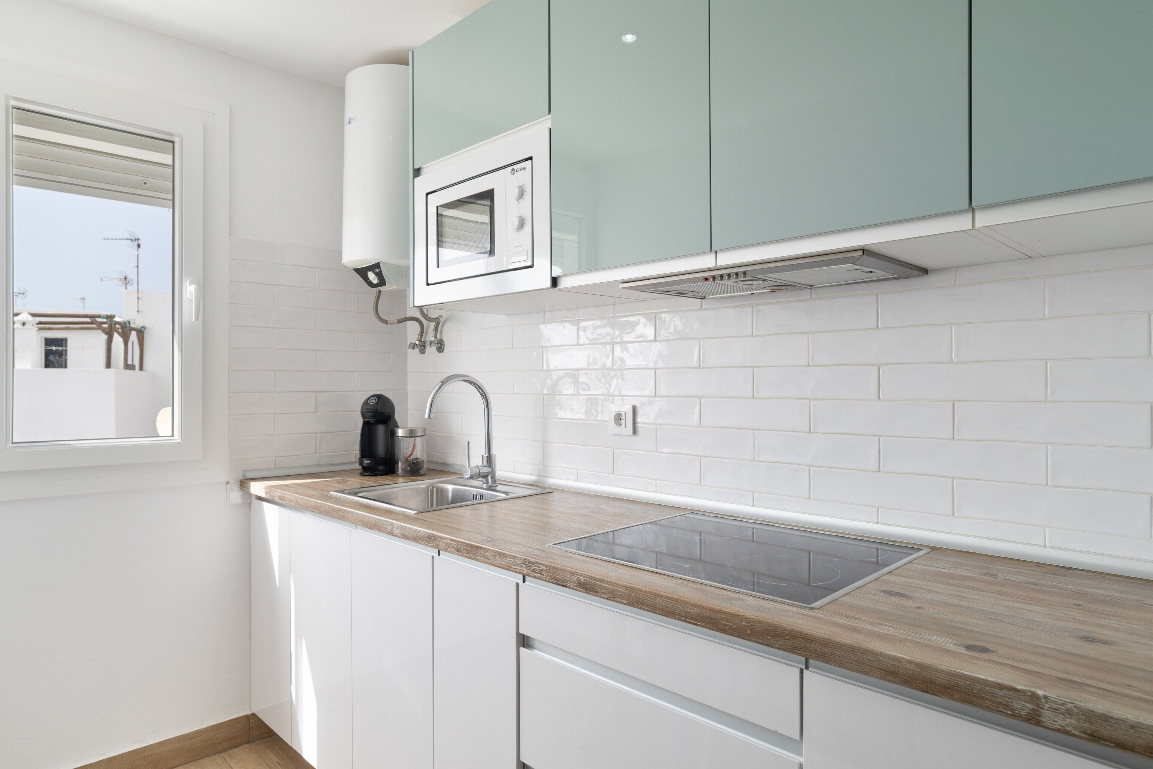 A modern kitchen with white cabinets, a wooden countertop, a built-in microwave, and a window.