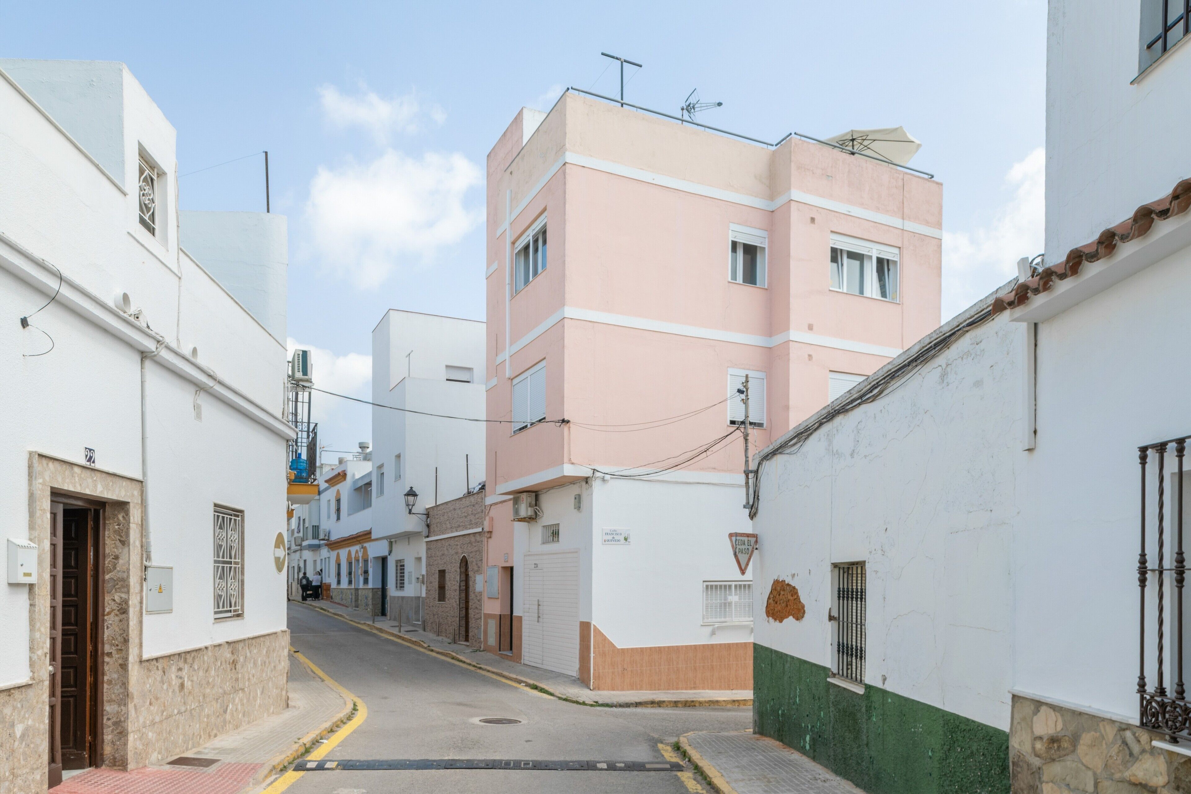 Une rue étroite bordée d’immeubles, l’un avec une porte et une fenêtre bien visibles, l’autre avec un balcon et une antenne parabolique.