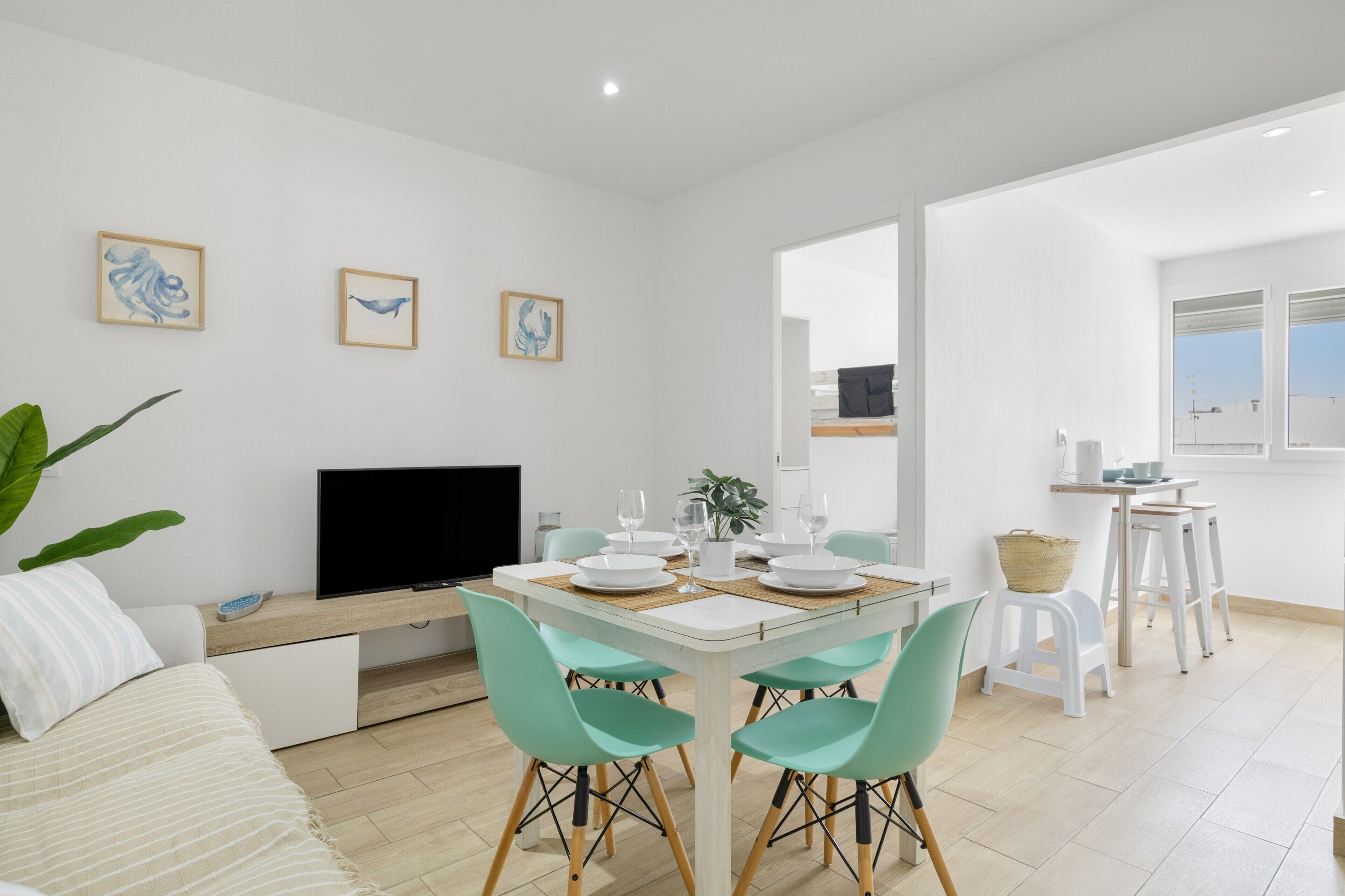 A modern living room with a dining area, a flat-screen TV, and artwork on the walls.