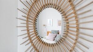 A room with a circular mirror, a bed with pillows, a bedside table, and a wall-mounted light fixture. - Apartment 'Almadraba' with Private Terrace, Wi-Fi and Air Conditioning (Barbate)