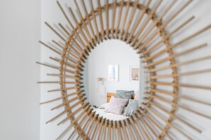 Una habitación con un espejo circular, una cama con almohadas, una mesita de noche y una lámpara fijada a la pared.