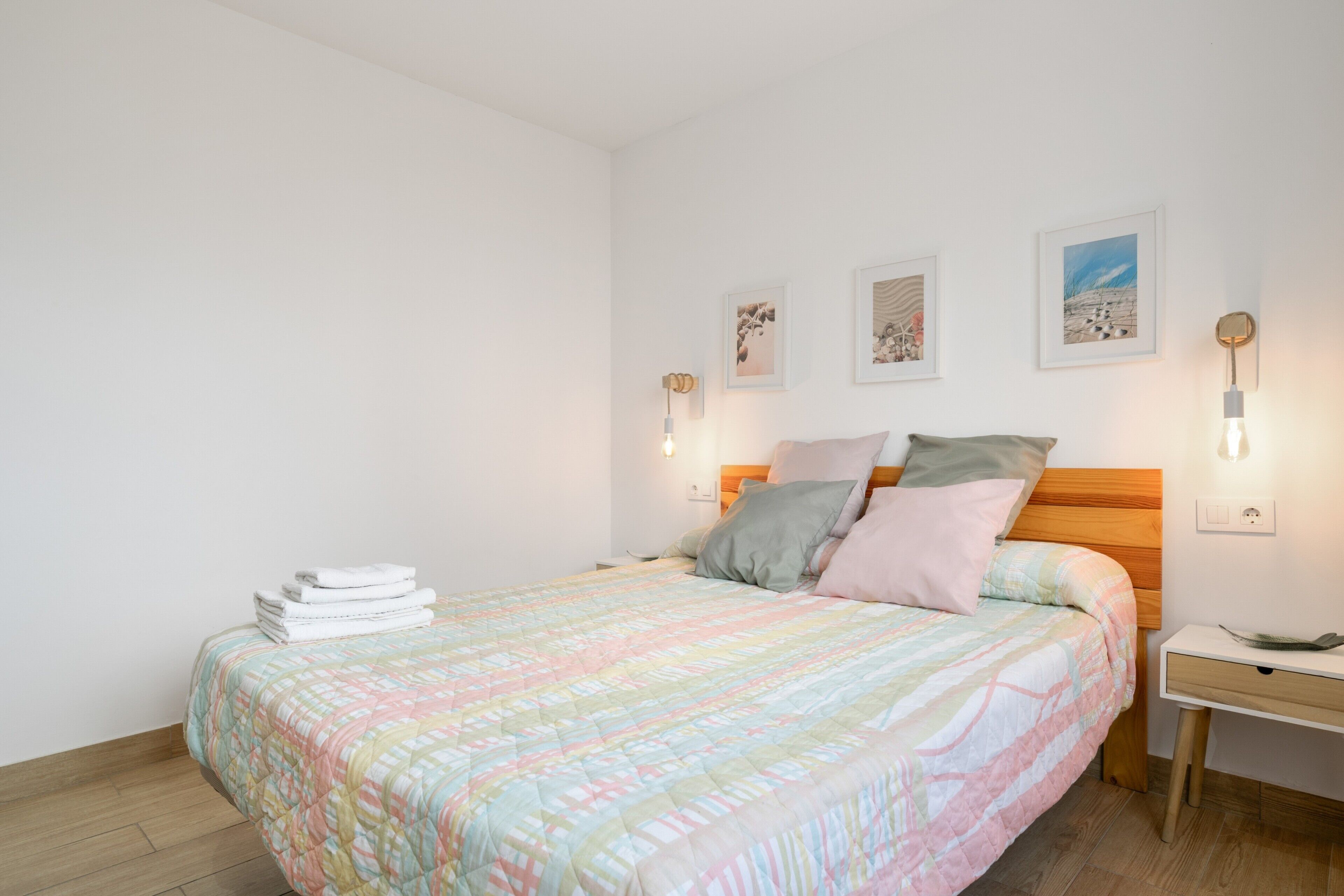 A neatly made bed with a colorful quilt, a bedside table with a lamp, and wall-mounted artwork.