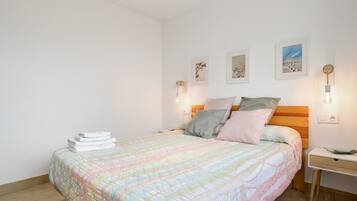 A neatly made bed with a colorful quilt, a bedside table with a lamp, and wall-mounted artwork.