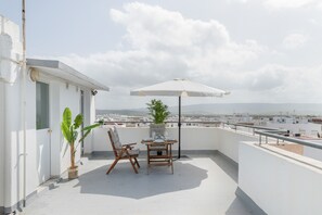 Una terraza en la azotea con una mesa para dos, una silla, una planta en maceta y una sombrilla.