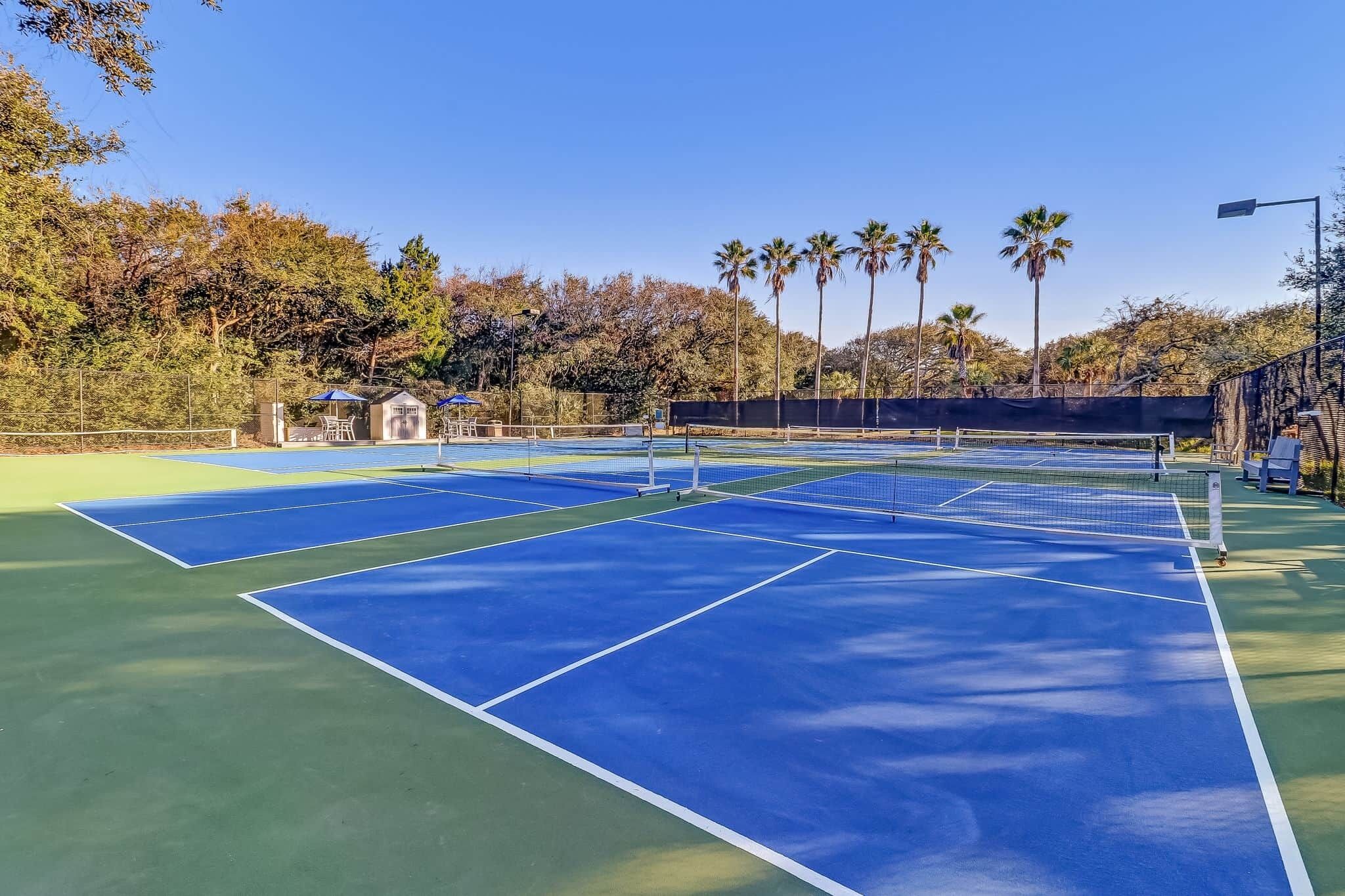 Un campo da tennis con più campi, un piccolo padiglione e palme sullo sfondo.