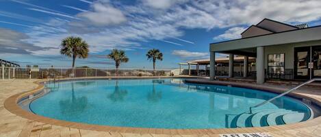 A swimming pool with a clear blue sky, palm trees, and a covered seating area.