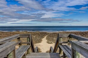 Un paseo marítimo de madera que lleva a una playa, con vista despejada al océano y al cielo.