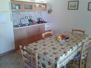 Een keuken met houten kastjes, een spoelbak, een fornuis en een eettafel met een bloemrijk tafelkleed.