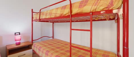 A bunk bed with a plaid bedspread, a bedside table with a lamp, and a drawer unit.