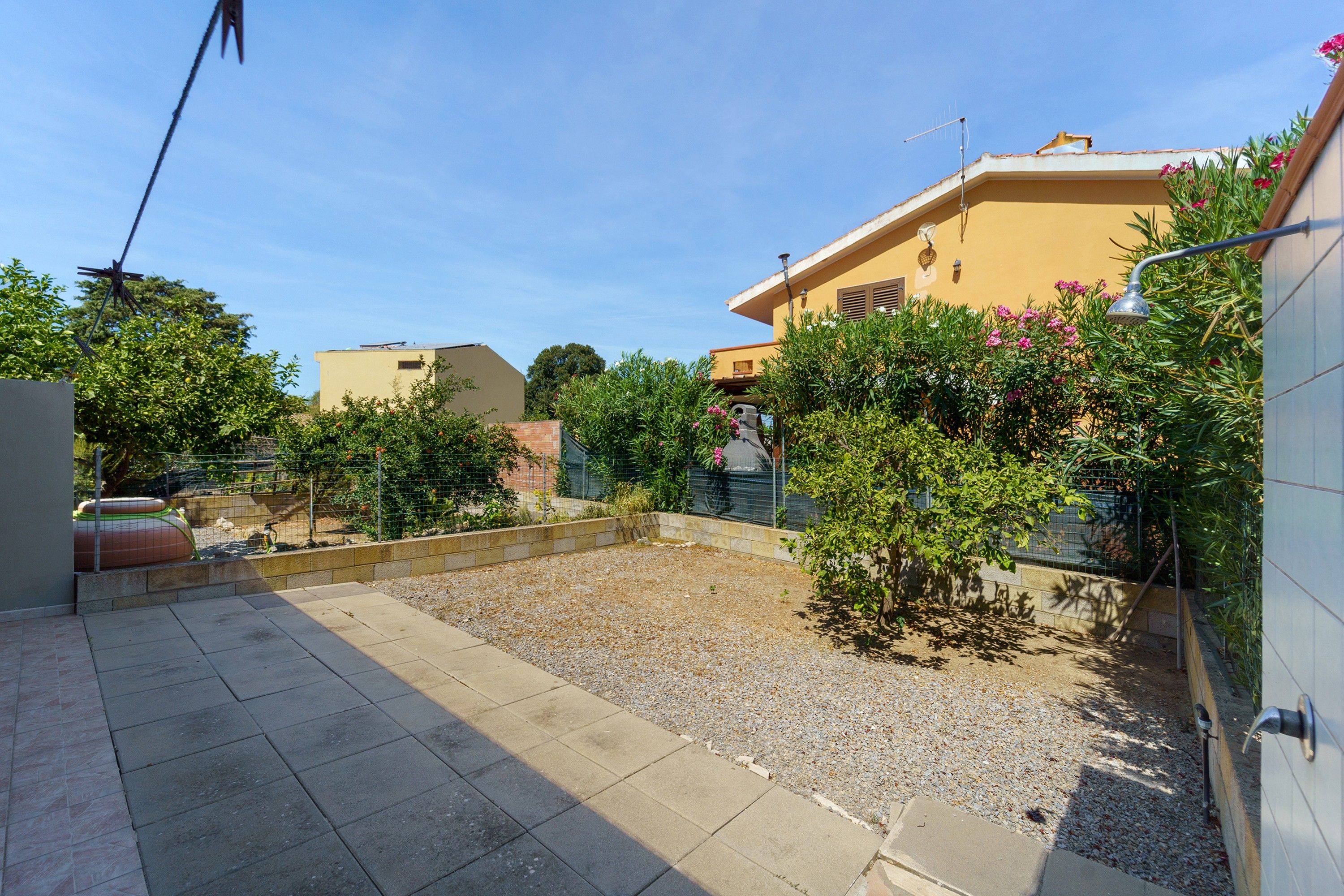 A courtyard with a paved area, a small garden with shrubs and flowers, and a building with a flat roof and a satellite dish.
