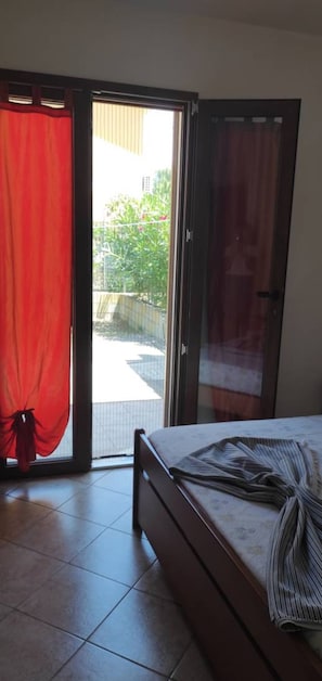 Een slaapkamer met een bed, een schuifdeur naar een balkon en een rood gordijn.