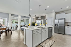 A modern kitchen with a central island, stainless steel appliances, pendant lighting, and a dining area with a view. - 5BR End-Unit w Pool  Themed Rooms   GameLoft 16225 (Clermont)