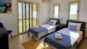 Un dormitorio con dos camas, un ventilador de techo, un cuadro y vistas por la ventana.