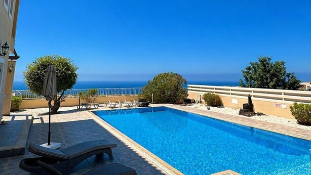 Una piscina con sillas de descanso, un suelo de baldosas y vista al mar.