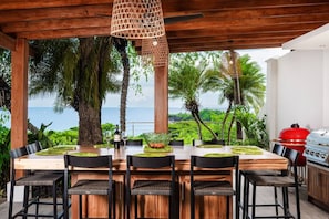 An outdoor dining area with a wooden table, chairs, and a grill. - Fabulous Ocean View Family Villa (Las Catalinas)