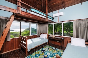 A room with a bed, a desk, and large windows offering a view of greenery and water. - Fabulous Ocean View Family Villa (Las Catalinas)