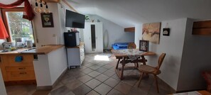 Uma cozinha compacta com frigor ífico embutido, uma mesa de jantar com cadeiras, uma televisão montada sobre a bancada e um guarda-roupa ao fundo.