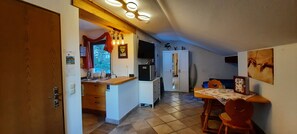 Eine Küche mit Holzarbeitsplatte, einem Esstisch mit Stühlen, einem Kühlschrank und einem an der Wand befestigten Fernseher.