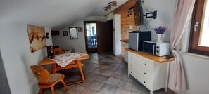 Uma cozinha compacta com mesa, cadeiras, geladeira e janela com cortinas.