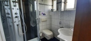 Ein Badezimmer mit Duschkabine, Toilette, Waschbecken und Spiegel.