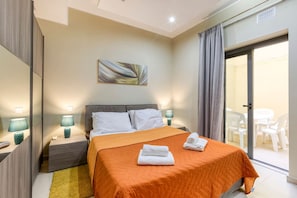 A hotel room with a bed, two bedside tables with lamps, a large window with curtains, and a view of the outside. - Marsaskala Escape | Pool, Beaches & Local Charm (Marsaskala)