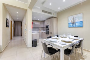 A dining area with a table set for six, a kitchen in the background, and a painting of a sailboat on the wall. - Marsaskala Escape | Pool, Beaches & Local Charm (Marsaskala)