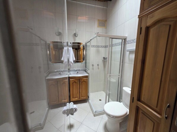 A bathroom with a glass shower enclosure, a toilet, and wooden cabinets. - Casa Hotel Realeza del Estádio (Medellín)