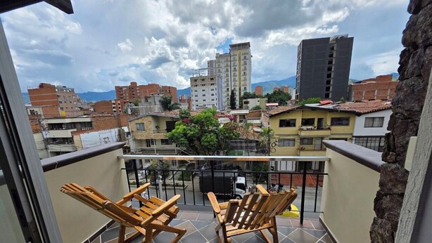 A balcony with two wooden rocking chairs, a tiled floor, and a view of surrounding buildings. - Casa Hotel Realeza del Estádio (Medellín)