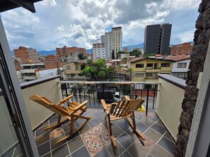 A balcony with two wooden rocking chairs, a tiled floor, and a view of surrounding buildings. - Casa Hotel Realeza del Estádio (Medellín)
