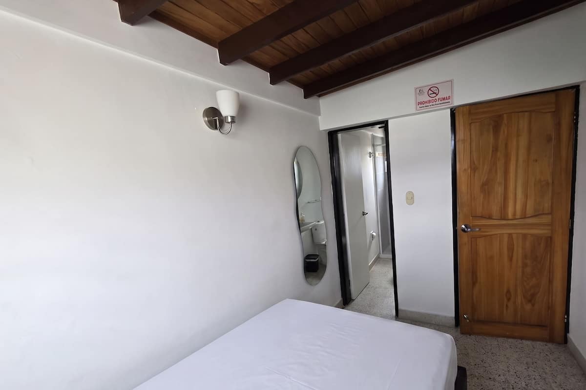 A bedroom with a bed, a wooden ceiling, a mirror, a door, and a sign prohibiting smoking.