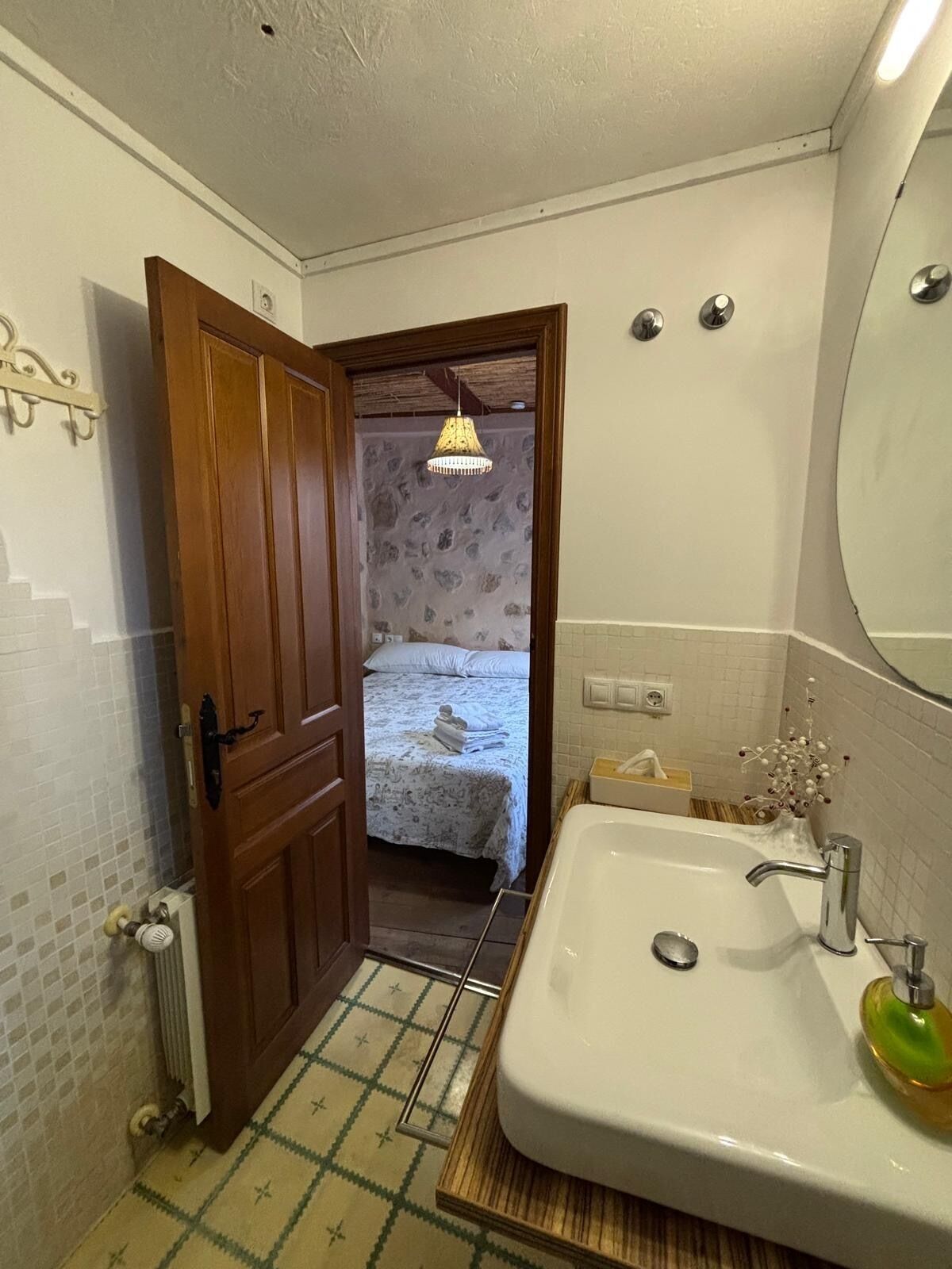 A bathroom with a wooden door, a white sink with a green soap dispenser, a towel rack, and a mirror.
