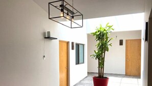 Un pasillo con un banco rojo, una planta en maceta, un extintor y puertas.