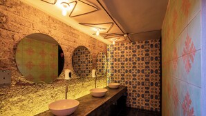 Un baño con tocador de madera, tres lavamanos, un espejo y baldosas estampadas.