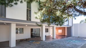 Un edificio con un espacio exterior cubierto, un acceso empedrado en piedra y un árbol.