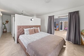 A bedroom with a large bed, a bedside table, a nightstand, a wall-mounted lamp, and a view into another room. - Damberde House, Damascus Resort, Jan Thiel (Jan Thiel)